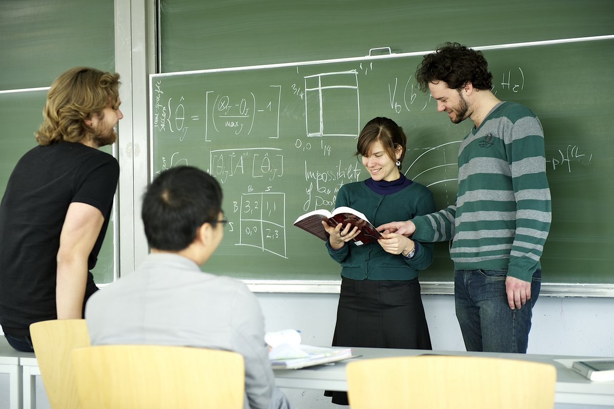 Vier Studierende in einem Seminar vor einer Tafel.